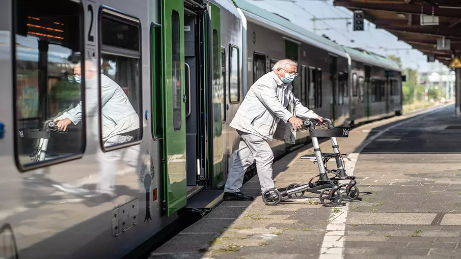 Ein älterer Mann mit Rollator steigt aus einem Zug aus